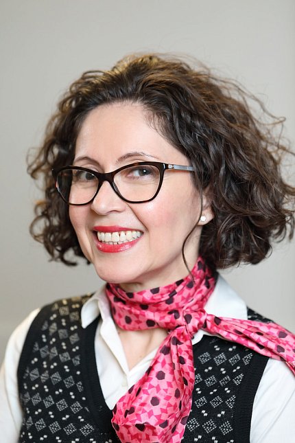 Dr. Mercedes Rubio wearing glasses, a pink scarf and a sweater vest over a white shirt