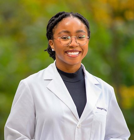 Megan Ezeude smiling in white lab coat with green background