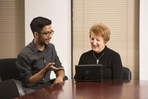An older adult looks at an iPad while a young man looks on