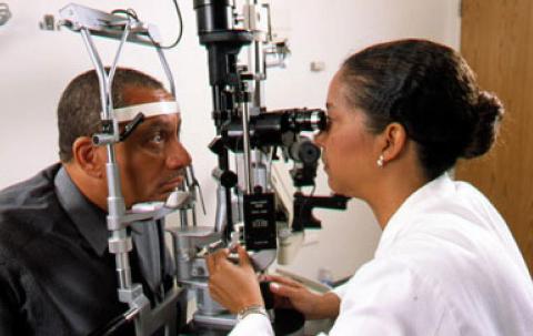 A man rests his chin on a diagnostic machine as optometrist examines his eyes.