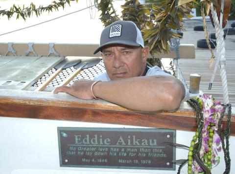 Kalepa rests his arm on edge of canoe, above plaque dedicated to the memory of Eddie Aikau