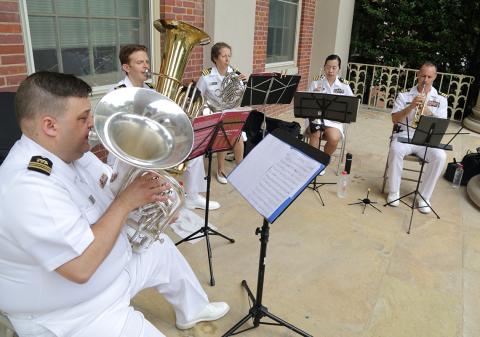 Musicians in their white uniforms play their brass instruments.