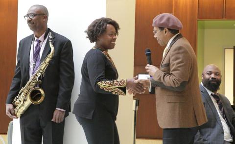 A fan shakes hands with bandleader while pianist and saxophonist look on.