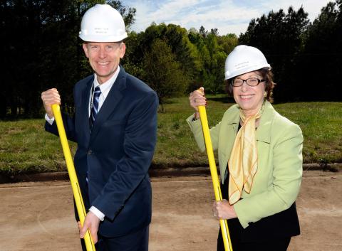 Wheeland and Birnbaum, wearing white hard hats, smile, holding shovels.