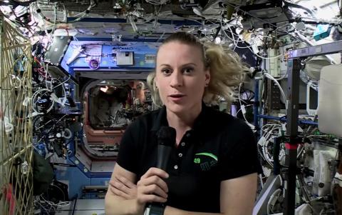 Dr. Kate Rubins talks into microphone inside space station, surrounded by wires and equipment.