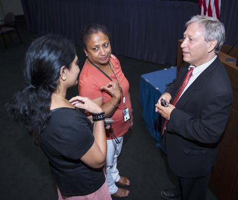 Wayne stands by podium talking with two attendees.