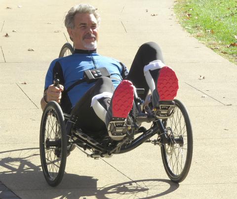 Michael McClellan rides on a tech-assisted three-wheeled recumbent cycle.