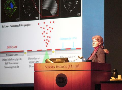 West at the NIH podium with slide projected beside her