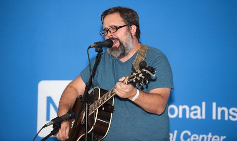 Milner playing guitar and singing at microphone