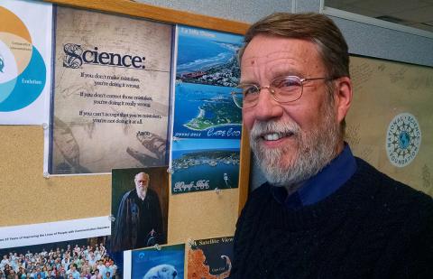 Dr. Christopher Platt stands in front of bulletin board with science posters.
