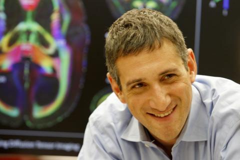 Reich smiles in front of a colorful MRI brain image