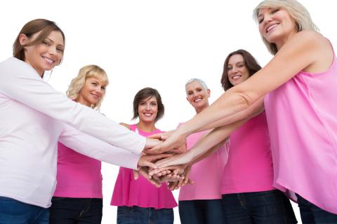 Six women wearing pink stack their hands together in unity