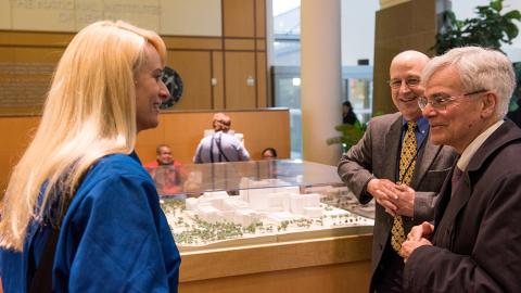 Gilman and Gottesman, standing next to Clinical Center model in the CC atrium, talk with Rubins