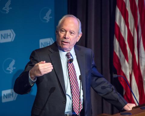 Leshner stands with hand cupped as he speaks at podium. 