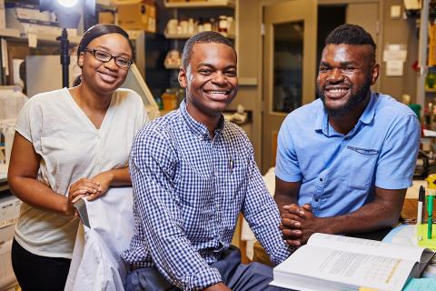 Three young people smile with a lab behind them