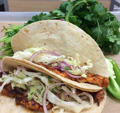 Two soft tacos filled with fish and onions sit on a bed of lettuce.
