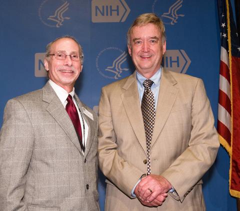 Dr. Robert Lembo and Sullivan pose together in front of blue NIH backdrop. 