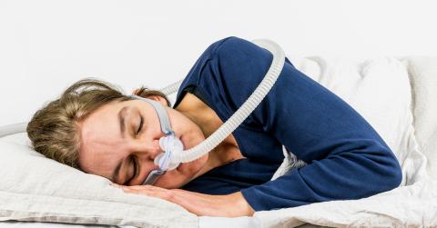 Woman sleeping on her side with CPAP, sleep apnea treatment.