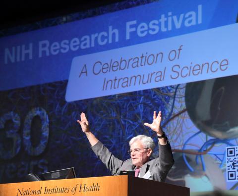 Dr. Gottesman holds hands up high at the podium, in front of slide that reads NIH Research Festival A Celebration of Science