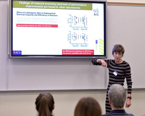 With slide projected behind her, Burke talks to seated attendees.