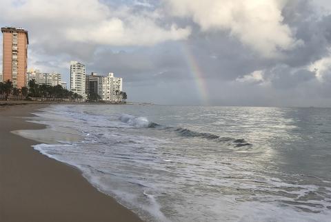 A rainbow shines through the clouds over a beach