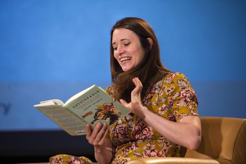 Thomson seated on stage reading from her book
