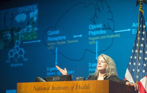 Kieffer gestures from the podium, with a slide projected behind her. 