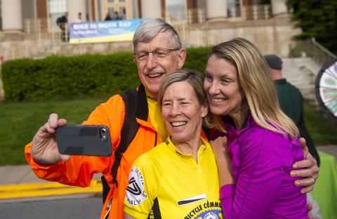 Dr. Collins hold out cell phone to take photo with his family in front of bldg. 1
