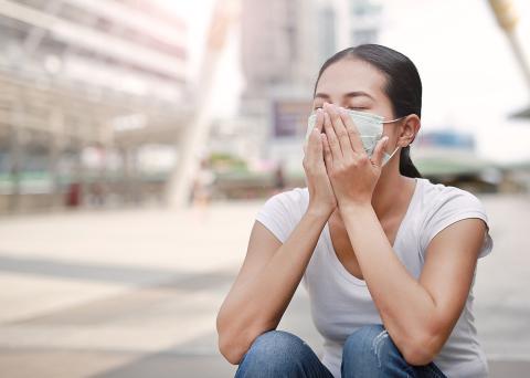 Woman in face mask with hands covering mouth