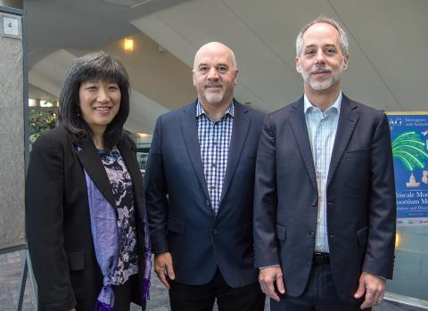 Three top meeting attendees stand smiling into camera