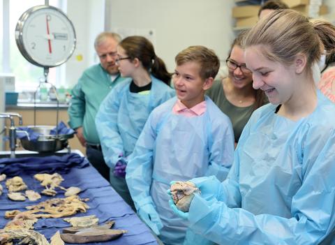 A smiling teenage girl wearing gloves holds a human organ in the autopsy suite.