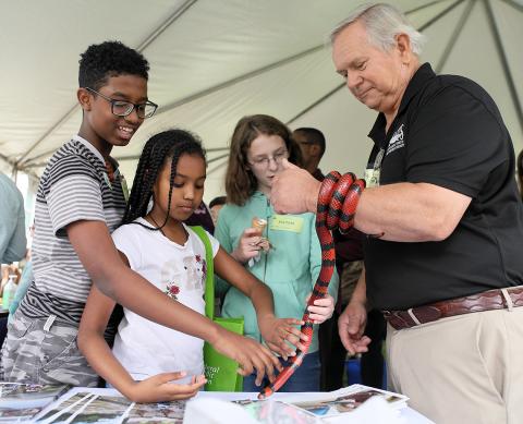 Kids pet a red and black snake that's wrapped around its owner's arm.