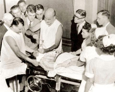 Black &amp; white image of Freeman, not in surgical scrubs or mask, performing lobotomy surrounded by onlookers.