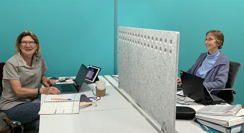 de Coronado and Walker face each other seated at telework desks. 