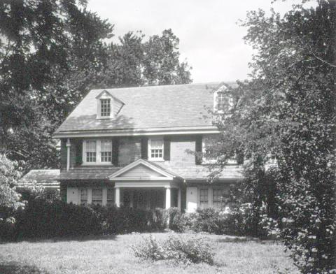 A 2-story house with yard, shrubs and trees