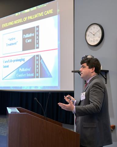 Shinall stands at podium in front of slide of evolving model of palliative care.