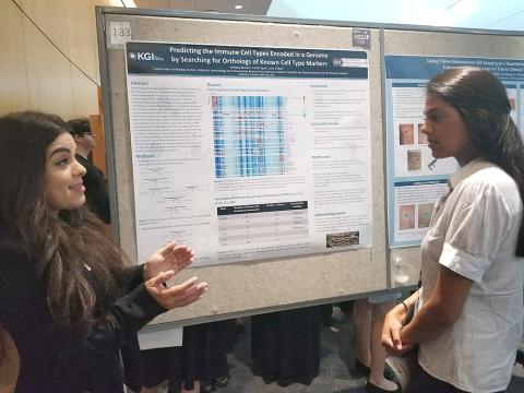 Murillo stands at poster, gesturing toward visitor.