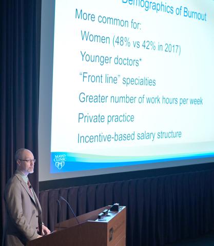 West at podium with slide of burnout demographics list projected beside him.