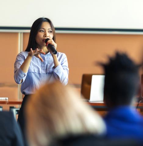 A woman standing speaks to an audience at a business presentation