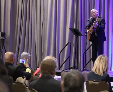 Dr. Collins stands on stage with his guitar singing into the mic to hundreds assembled in the Hyatt ballroom.