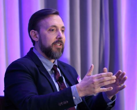 Rieder, seated on stage, speaks with hands raised.