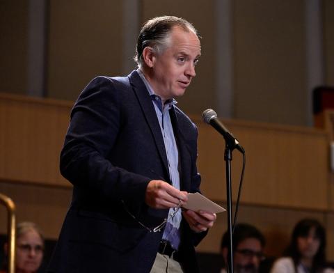 Standing at the microphone, David Dye has a quizzical look as he reads an anonymous audience question.