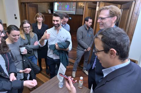 Several people gather around a man holding a smartphone.