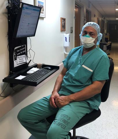 Dr. Chinquee in a mask and scrubs sits by a computer in a Clinical Center hallway.
