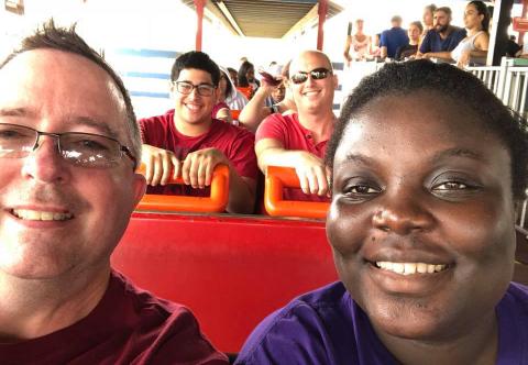 Jason and Chris, each seated next to a young adult they previously fostered, on a roller coaster.