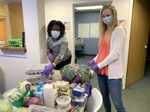 Two masked women at counter loaded with groceries.