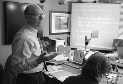 A black &amp; white photo of Dr. Remondini standing near a presentation slide in a conference room