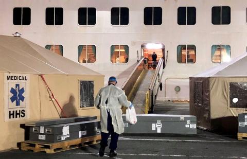 A responder in mask and gown holding a plastic bag walks onto a cruise ship.