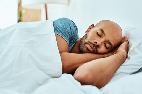 An African American man lays asleep in bed.