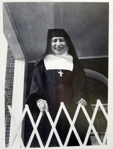 Sister Mary Rita in habit smiles from upper floor room balcony